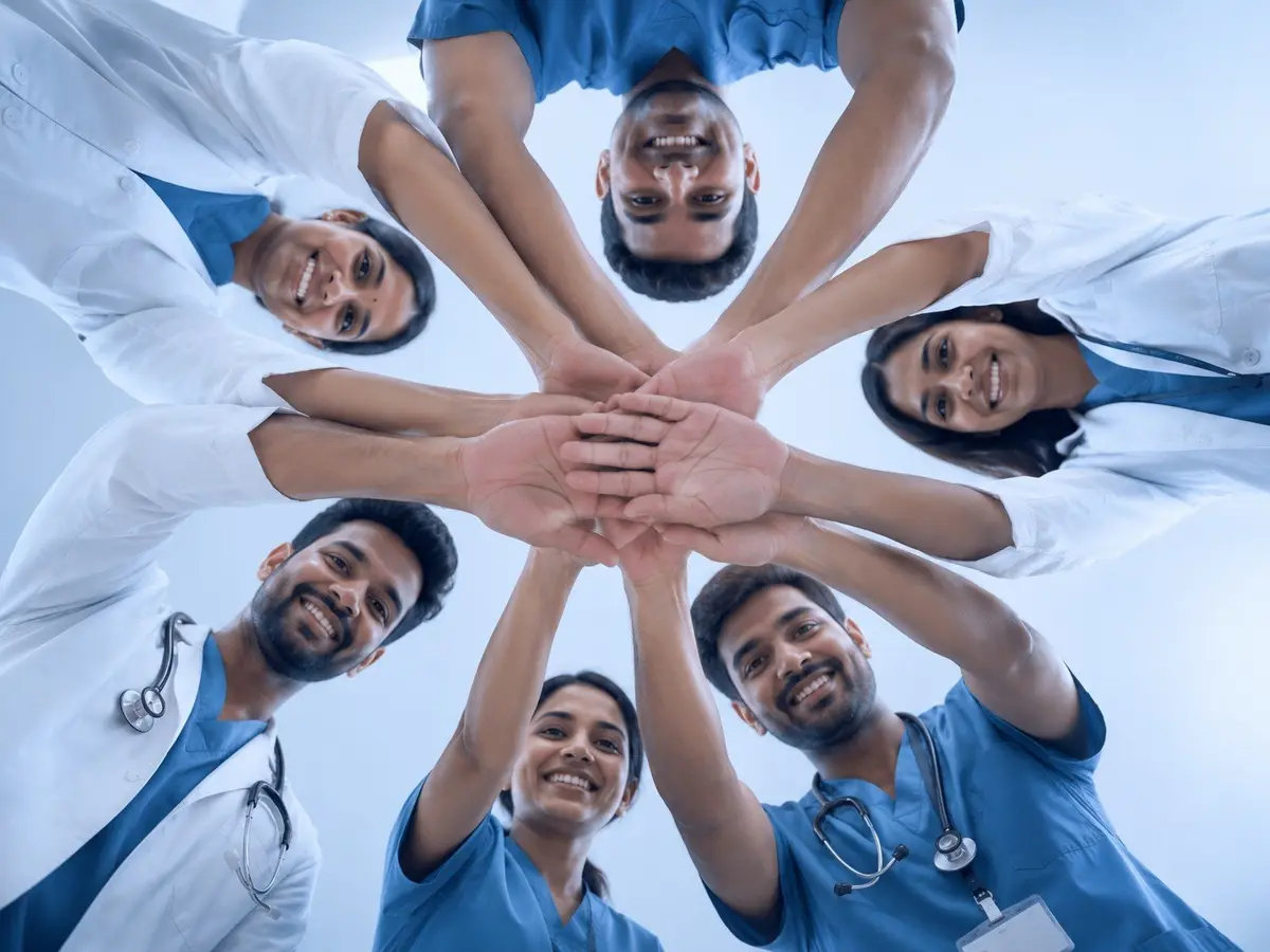 Young doctors and nurses joining hands in a circle, seen from below